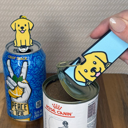 A matching set of Yellow Labrador-inspired Tab Buddies are shown. The soda-sized Tab Buddy rests atop a blue soda can, and the Tab Buddy XL is used to peel back a can of dog food.