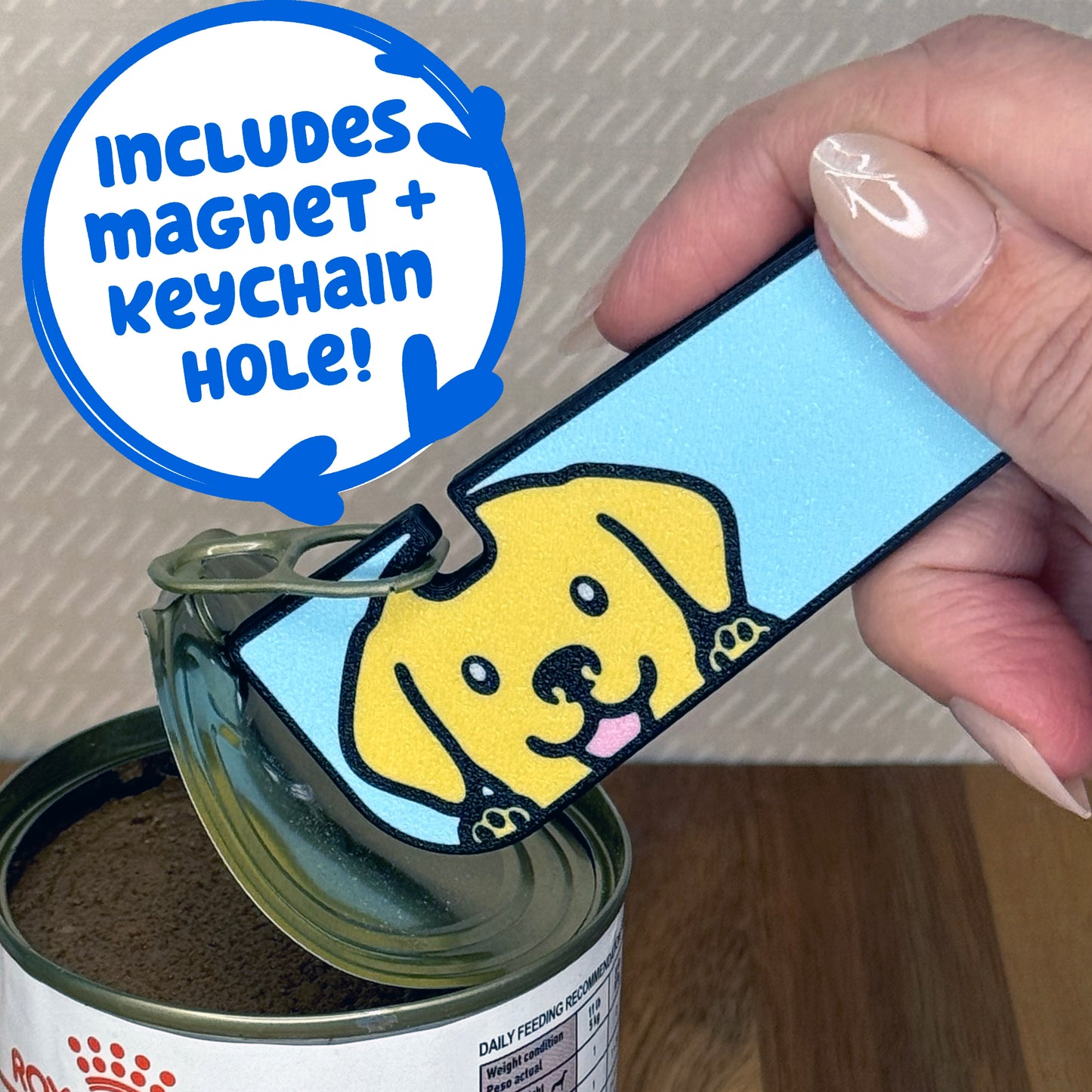 A Yellow Lab-inspired Tab Buddy XL is used to peel back the lid of a can of dog food. Descriptive text reads "Includes Magnet + Keychain Hole!"
