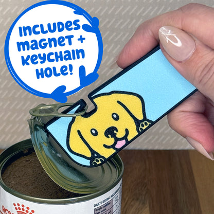 A Yellow Lab-inspired Tab Buddy XL is used to peel back the lid of a can of dog food. Descriptive text reads "Includes Magnet + Keychain Hole!"
