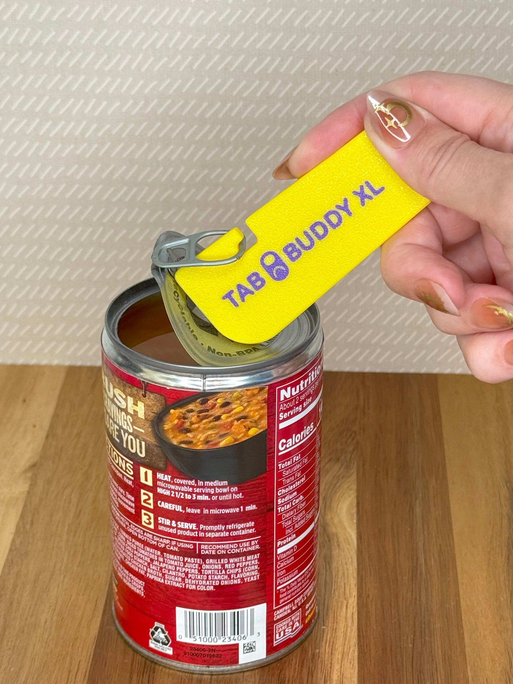 Hand using a lemon yellow and purple Tab Buddy XL can opener on a can of food with a red label.