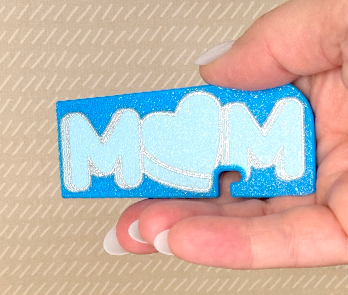 Hand holding a blue 'MOM' Tab Buddy XL against a beige background
