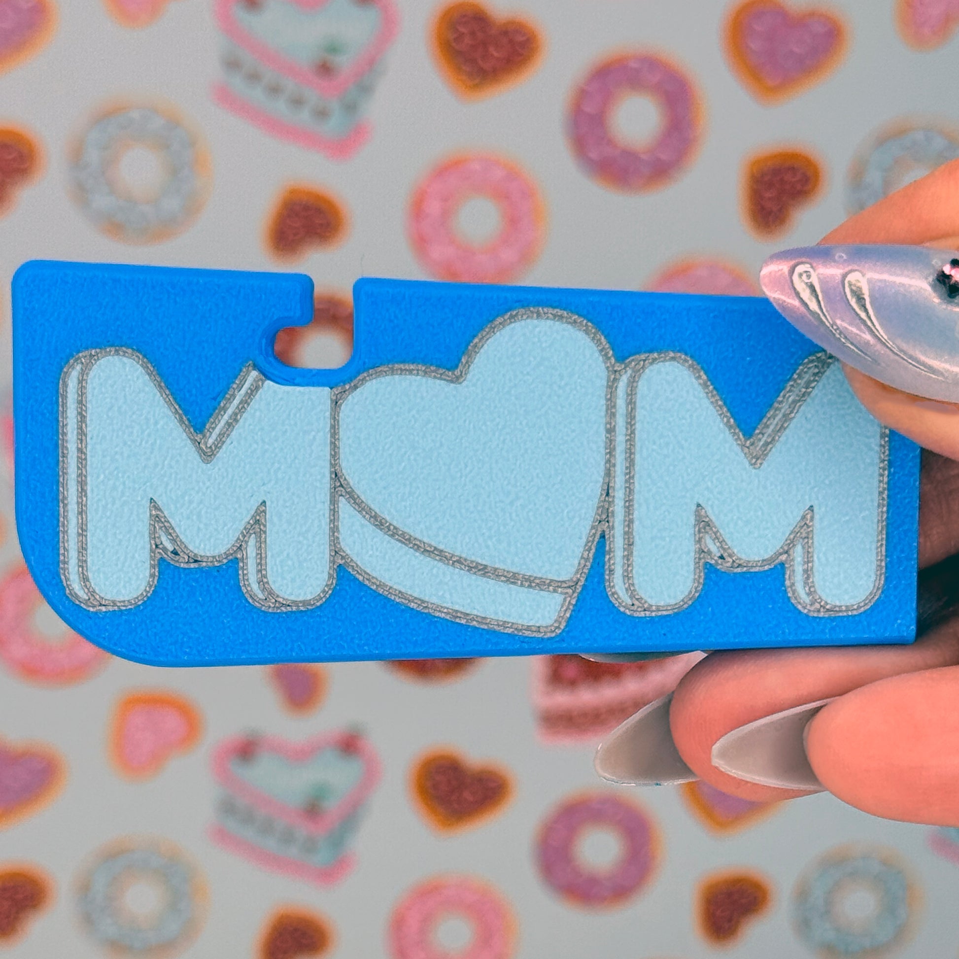 Blue Tab Buddy XL with 'MOM' written on it and a heart-shaped "O" held by a hand against a colorful background.
