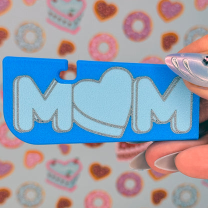 Blue Tab Buddy XL with 'MOM' written on it and a heart-shaped "O" held by a hand against a colorful background.