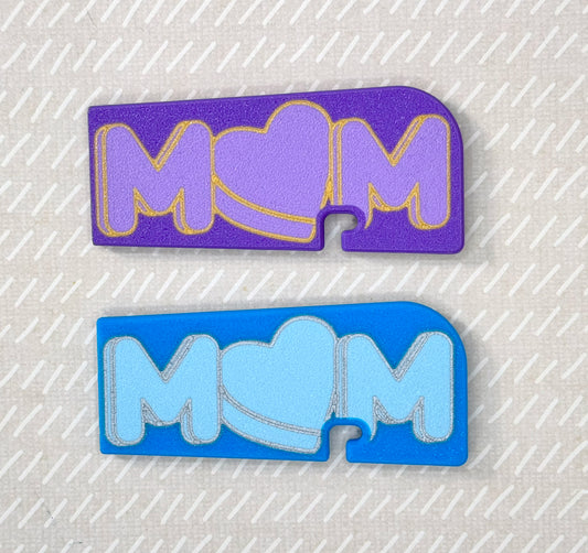Two 'MOM' Tab Buddy XLs, one purple and one blue, on a textured gray background.