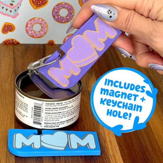 Hand using a Tab Buddy XL with 'MOM' text on a wooden surface and donut-themed wallpaper. Text box states, "includes magnet + keychain hole!"
