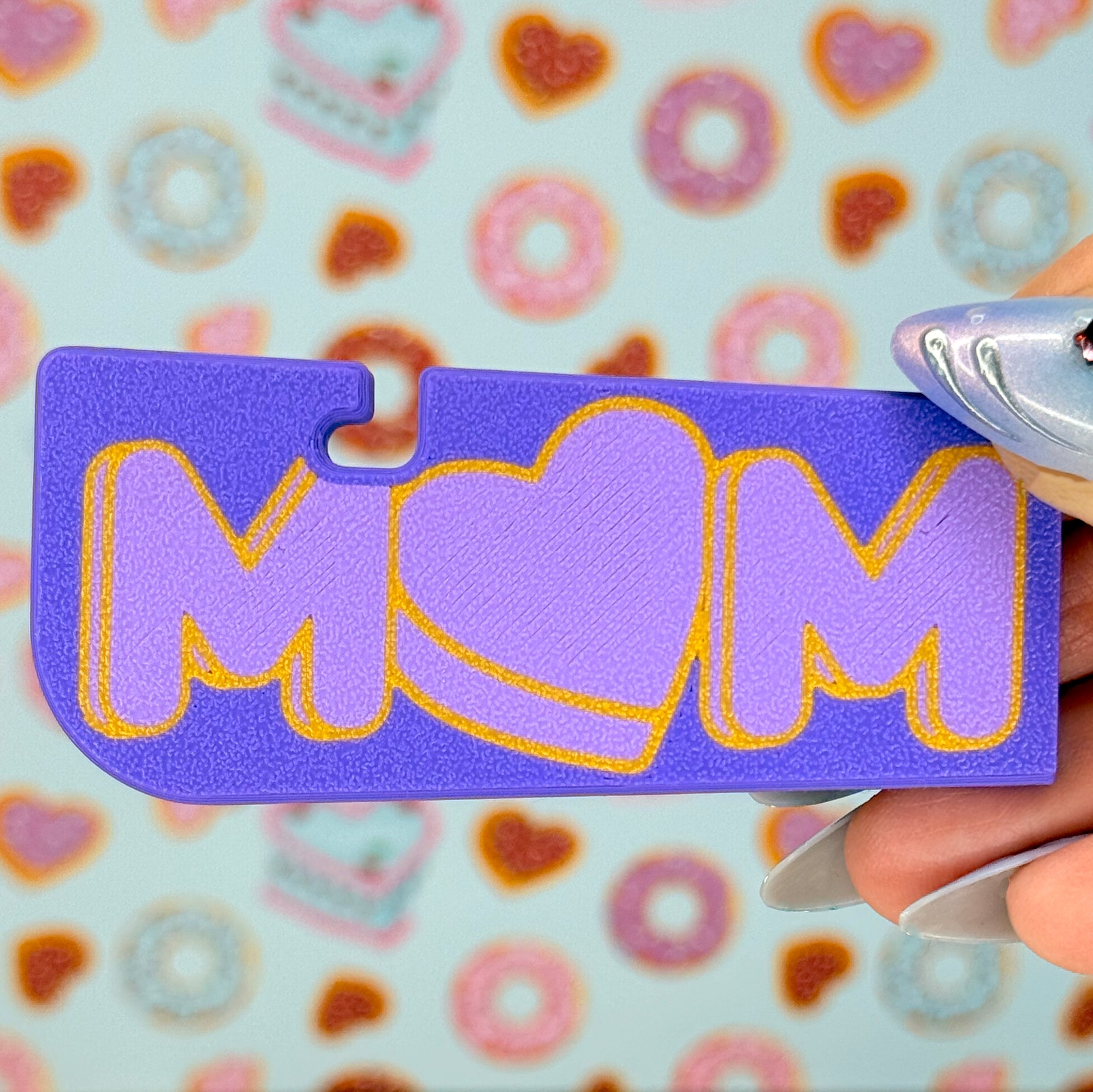 Purple Tab Buddy XL with 'MOM' written on it and a heart-shaped "O" held by a hand against a colorful background.