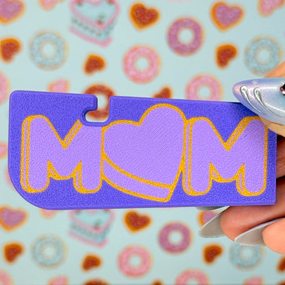 Purple Tab Buddy XL with 'MOM' written on it and a heart-shaped "O" held by a hand against a colorful background.
