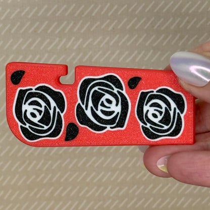 Red Tab Buddy XL with black rose patterns held by a hand against a beige background