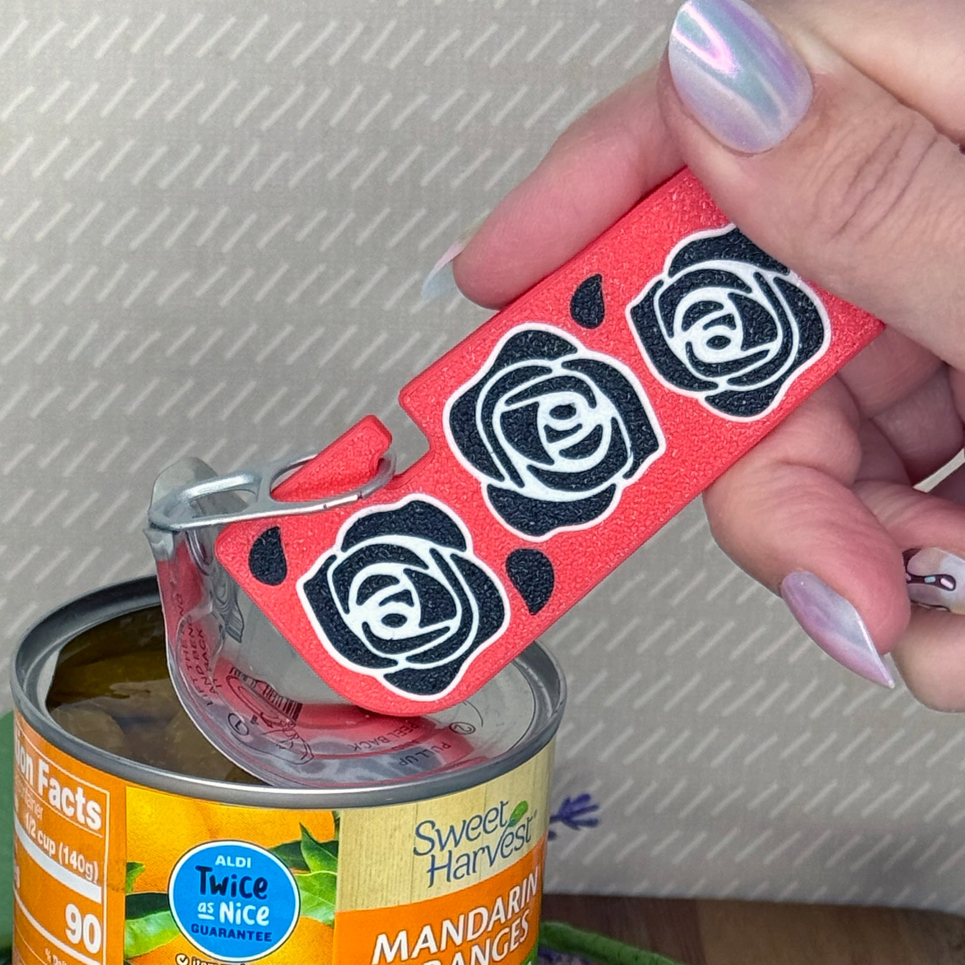 Hand using a red Tab Buddy XL with black rose designs on a can of Sweet Harvest mandarin oranges.