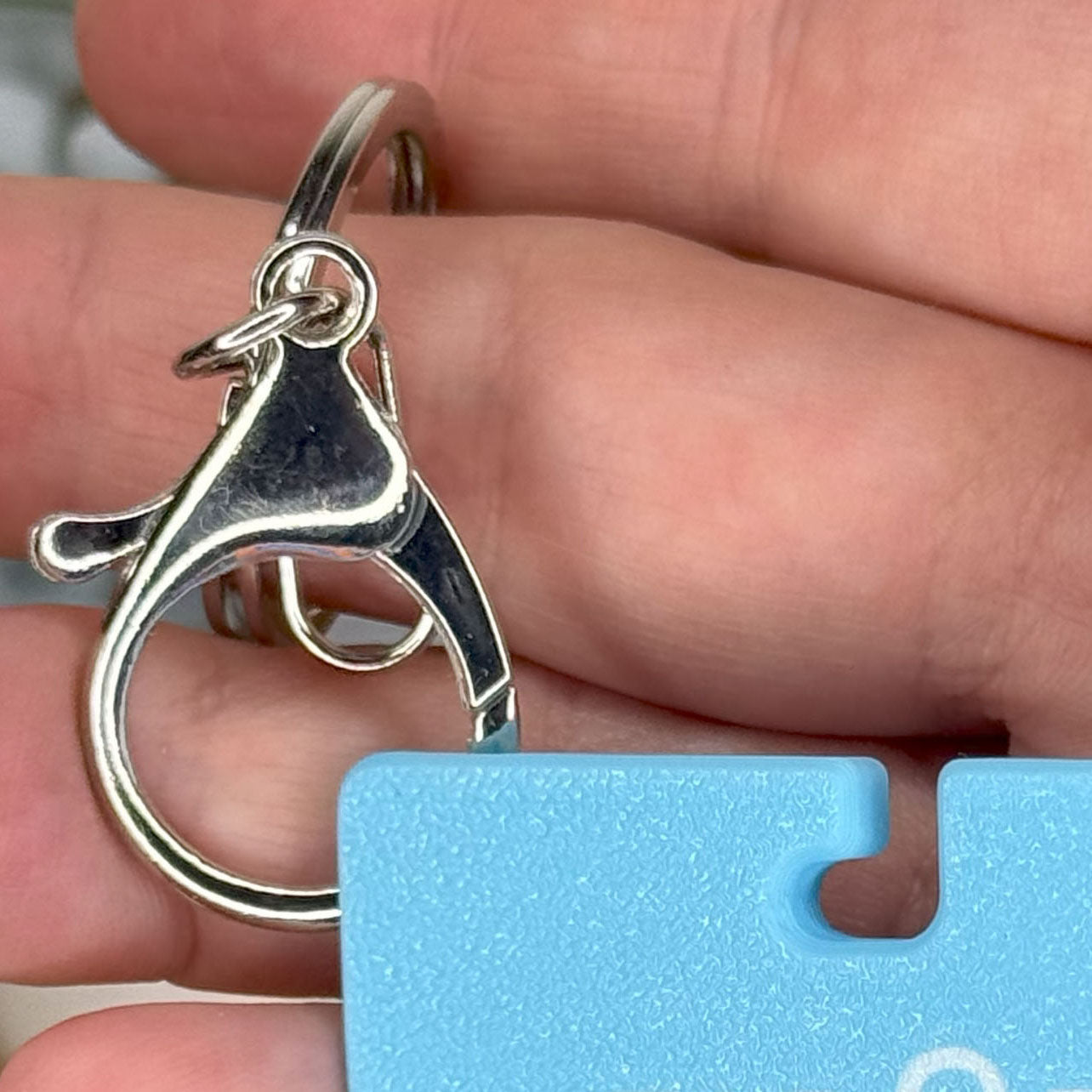 Silver keychain held between fingers with a blue Tab Buddy XL in the foreground