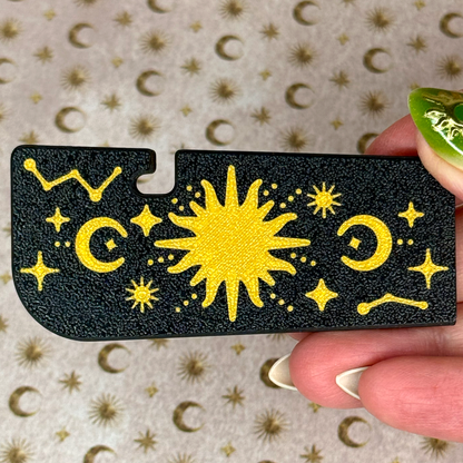 Black Tab Buddy XL with gold celestial designs held by a hand against a patterned background