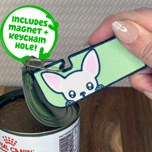 A cream Chihuahua-inspired Tab Buddy XL is used to peel back the lid of a can of dog food. Descriptive text reads "Includes Magnet + Keychain Hole!"