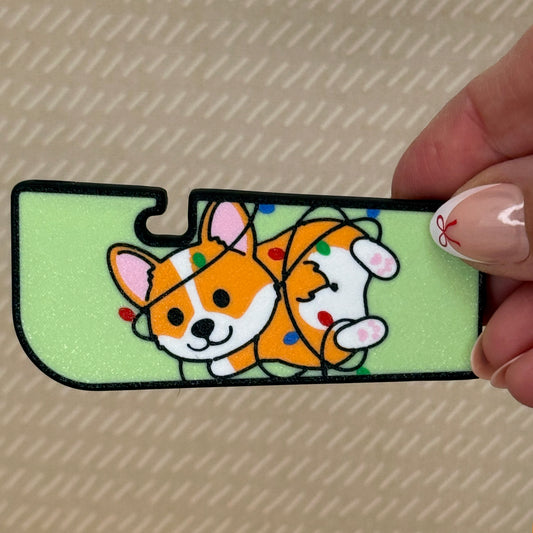 Hand holding a colorful Tab Buddy XL with a cartoon corgi wrapped in Christmas lights design with a light green background