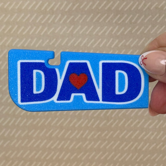 Blue 'DAD' Tab Buddy XL with a red heart is held by a hand on a beige background