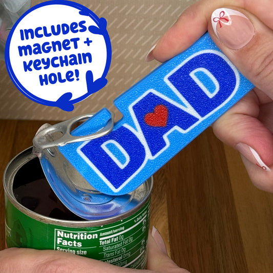 Blue 'DAD' Tab Buddy XL is used to open a vegetable can. Text notes the Tab Buddy XL includes a magnet and keychain hole.