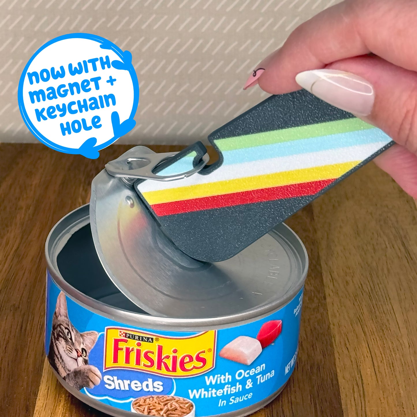 Person using a colorful Tab Buddy XL to open a can of Purina Friskies cat food, text reads 'now with magnet + keychain hole'