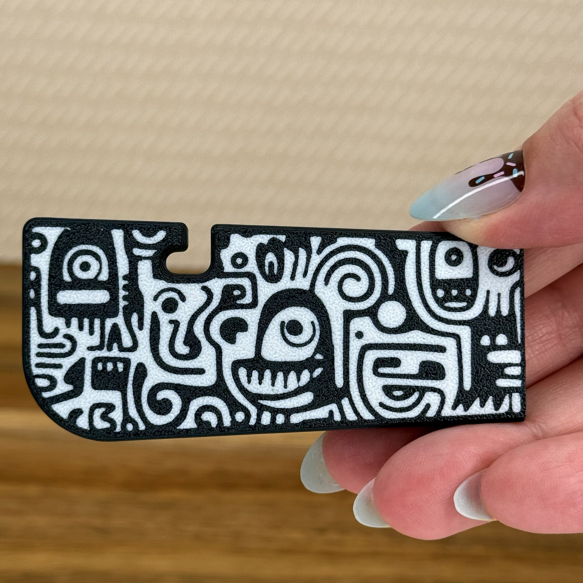 Hand holding a black and white doodle pattern Tab Buddy XL against a beige background