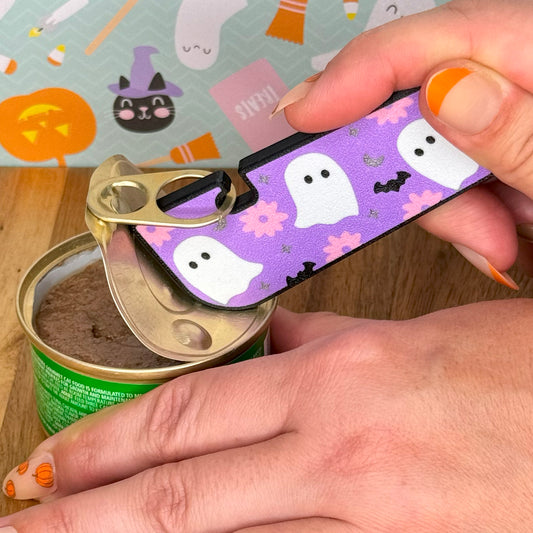 Halloween-themed Tab Buddy XL is used to open a can of cat food with a colorful background featuring pumpkins and ghosts.