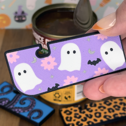 Halloween-themed Tab Buddy XL with ghosts and flowers on a purple background held by a hand over a can.