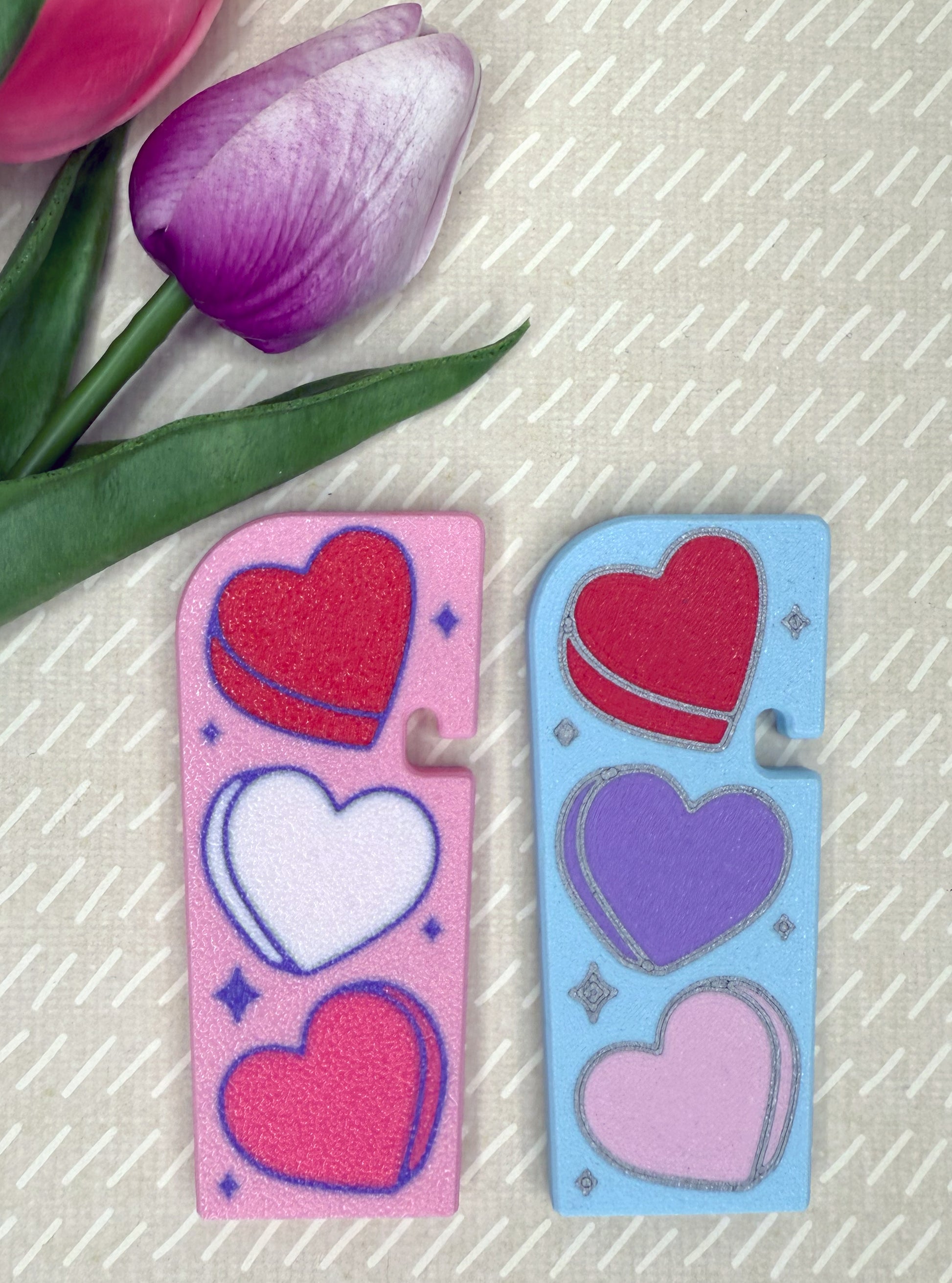 Two Tab Buddy XLs with colorful hearts on a textured surface with purple tulips.