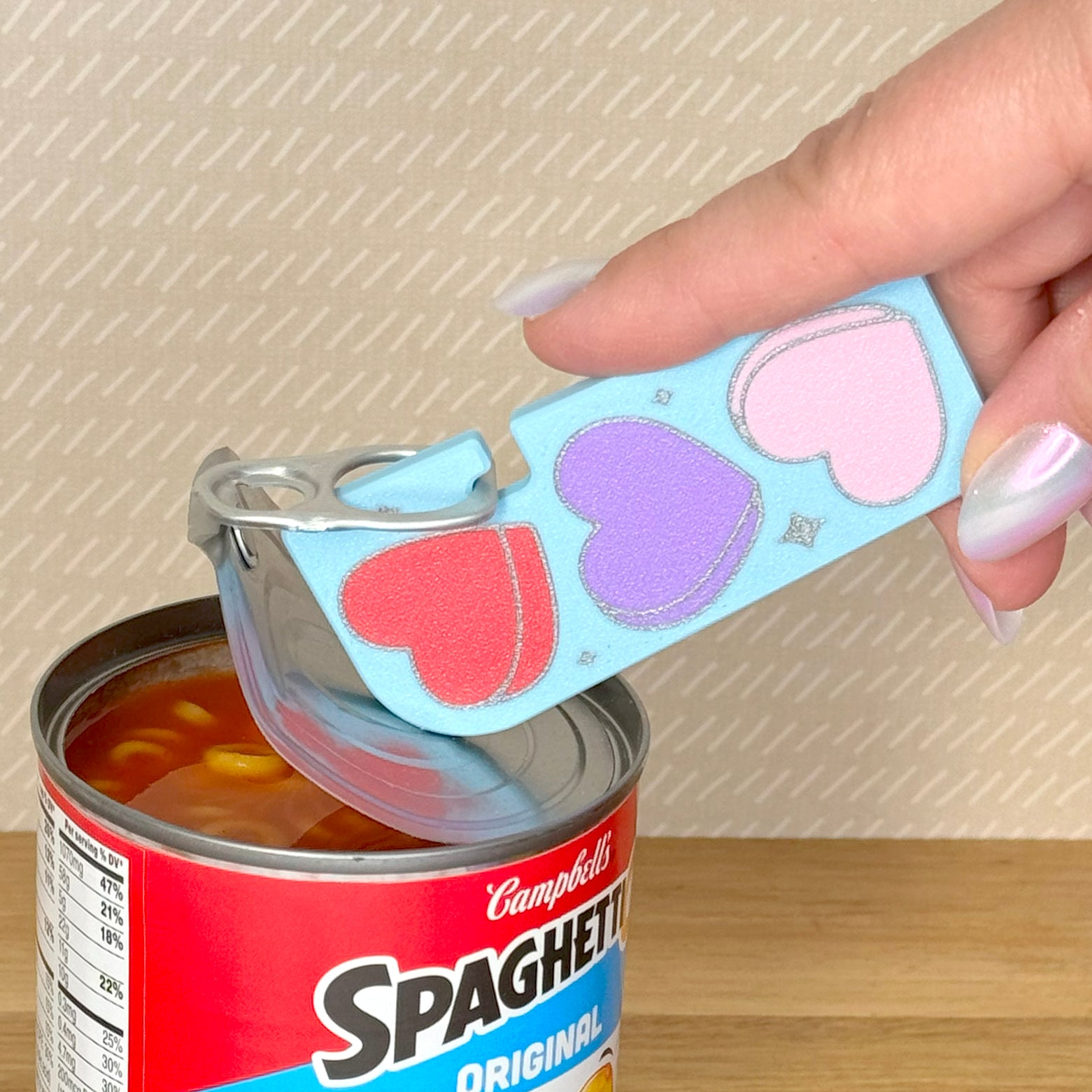Hand using a Tab Buddy  XL can opener with heart designs on a Campbell's Spaghetti-Os can.