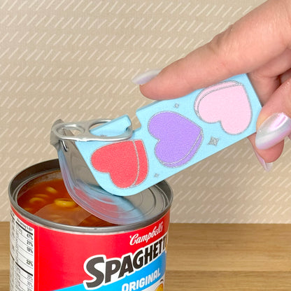 Hand using a Tab Buddy  XL can opener with heart designs on a Campbell's Spaghetti-Os can.