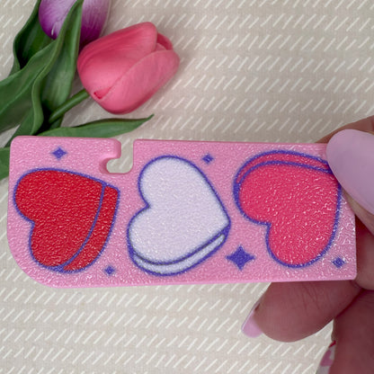 Pink Tab Buddy XL with heart designs held by a hand, with pink tulips in the background.