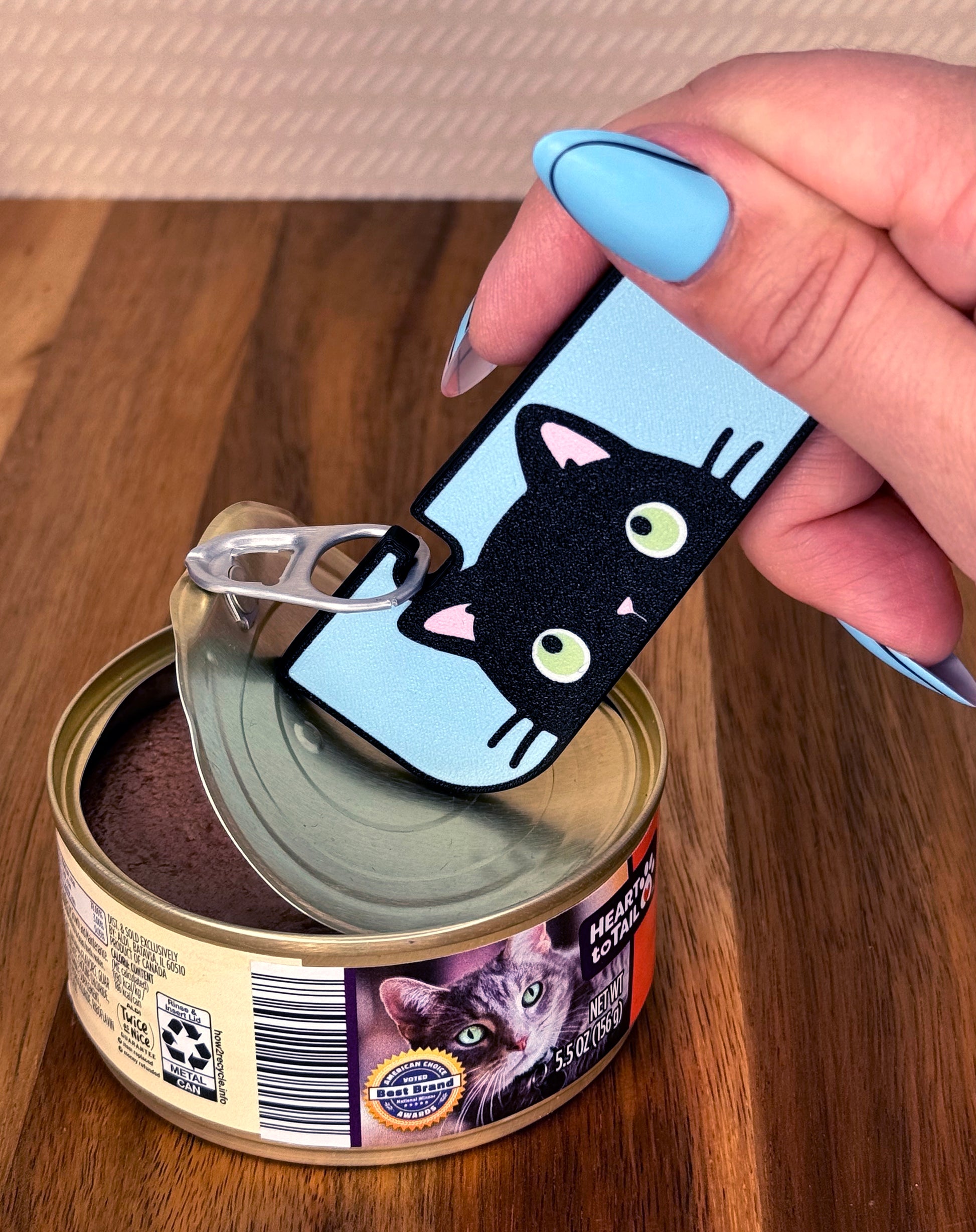 Hand using a black cat-themed Tab Buddy XL opening a can of cat food.