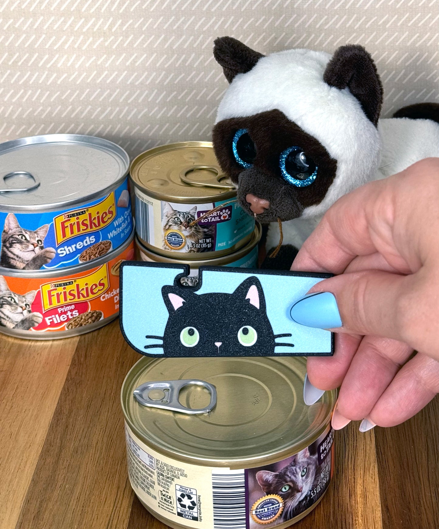 Person holding a black cat-themed Tab Buddy XL next to cat food cans on a wooden surface.