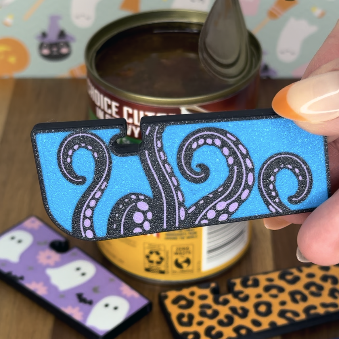 Person holding a blue and black Tab Buddy XL with tentacle design over a can.