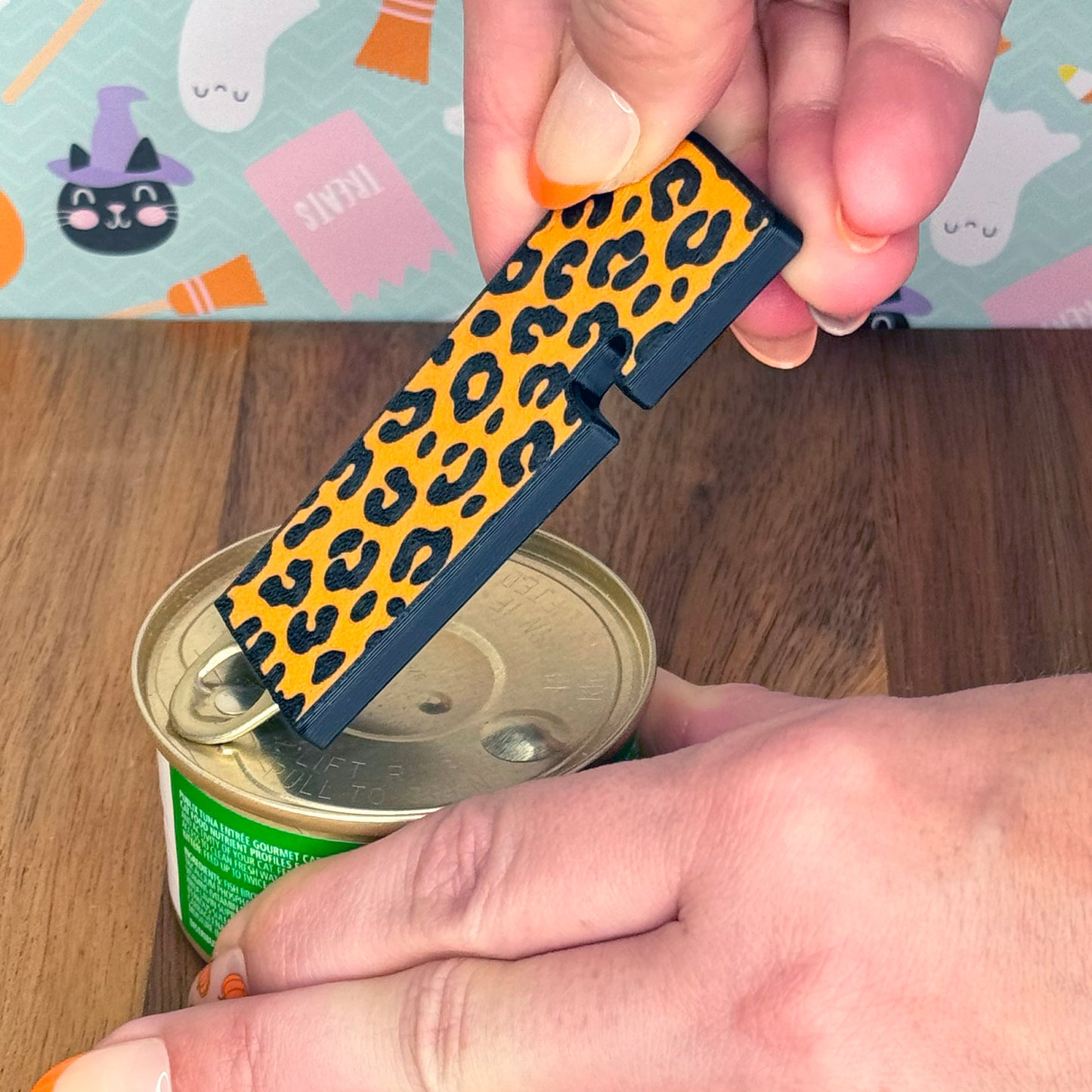 Person using an orange leopard print Tab Buddy XL to lift the tab on a can.