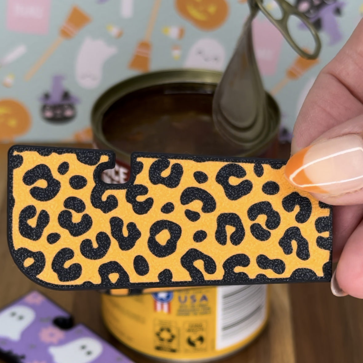 Hand holding an orange leopard print Tab Buddy XL with Halloween-themed background