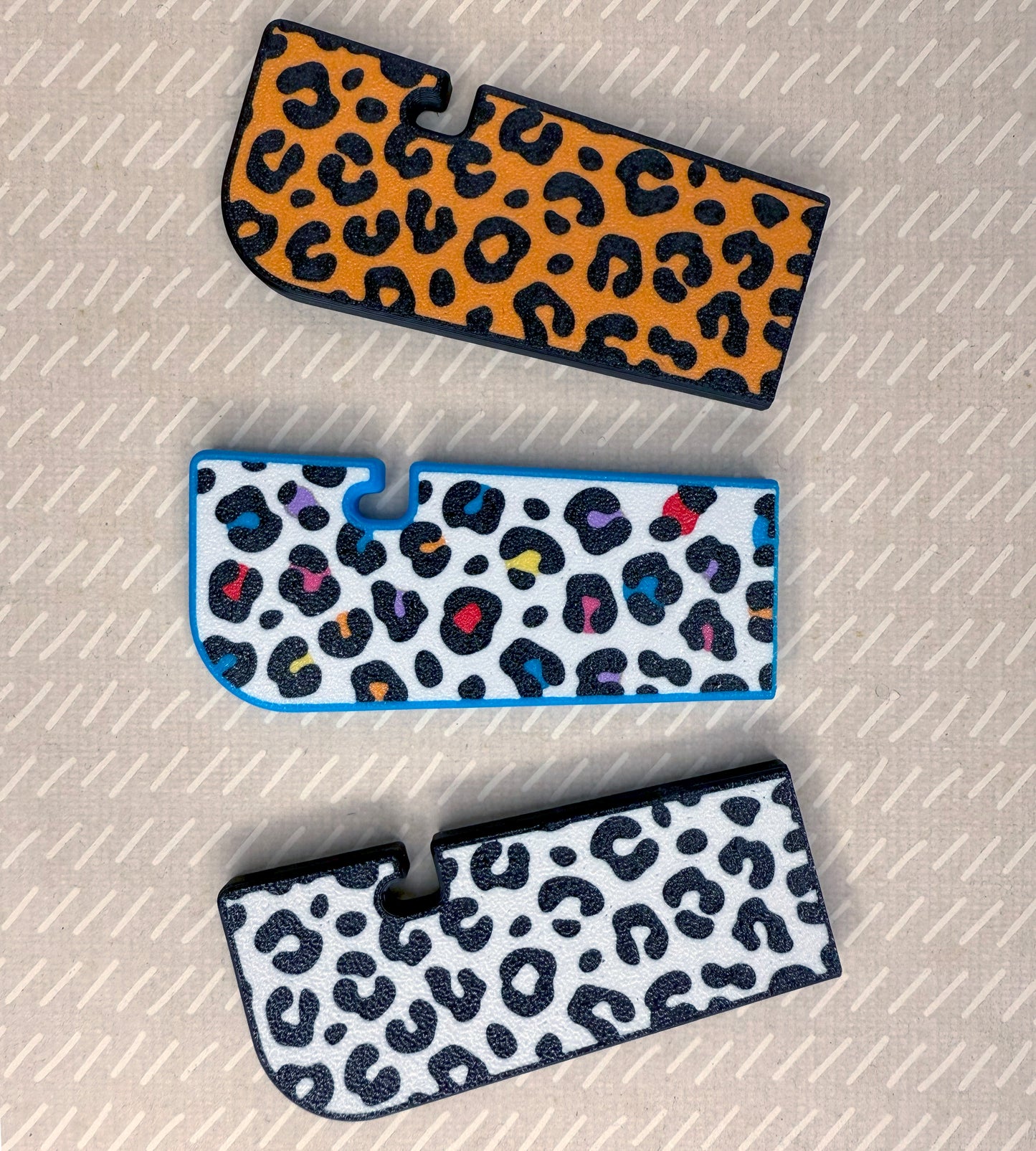 Three Tab Buddy XLs with variations or orange, rainbow and white leopard prints on a textured surface.