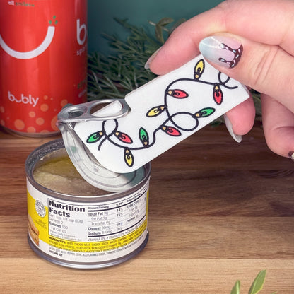 Hand using a Tab Buddy XL with Christmas lights design on a can of food.