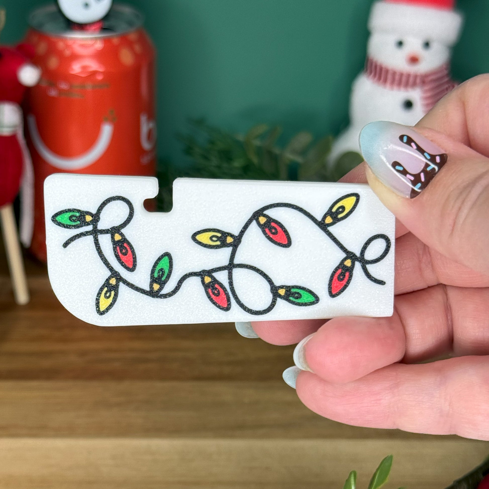 Hand holding a white Tab Buddy XL with Christmas lights design in front of a festive background.