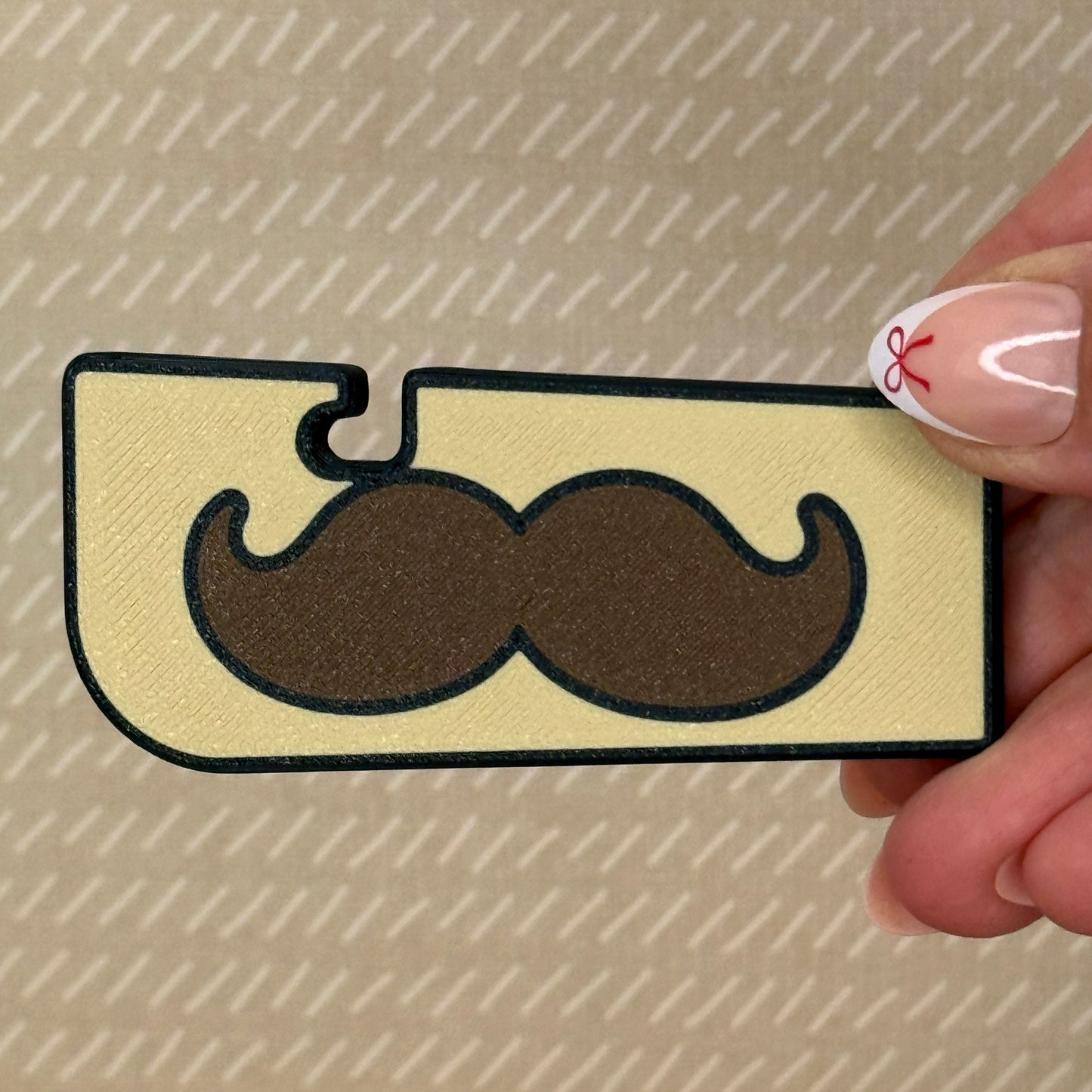 Beige Tab Buddy XL with a brown mustache design is held by a hand on a beige background