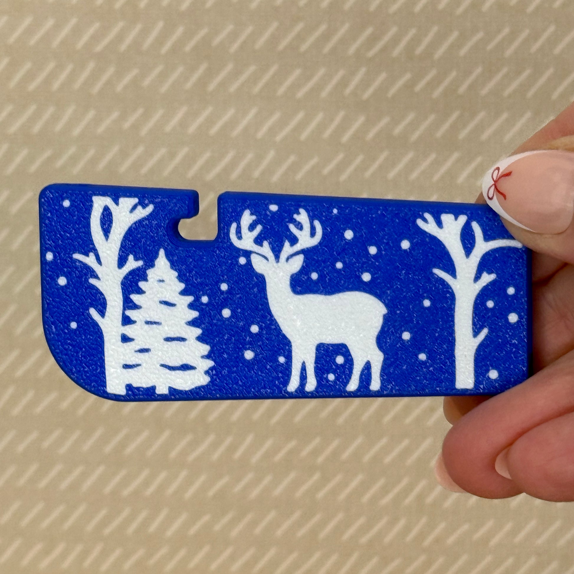 Blue Tab Buddy XLwith white deer, snow and tree design held by a hand against a beige background