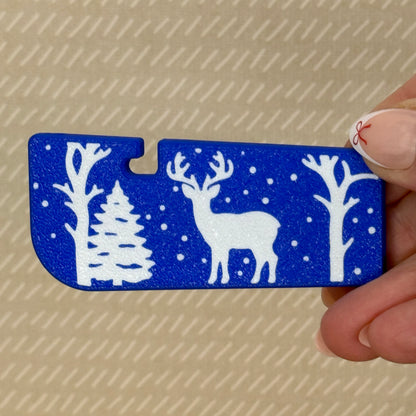 Blue Tab Buddy XLwith white deer, snow and tree design held by a hand against a beige background