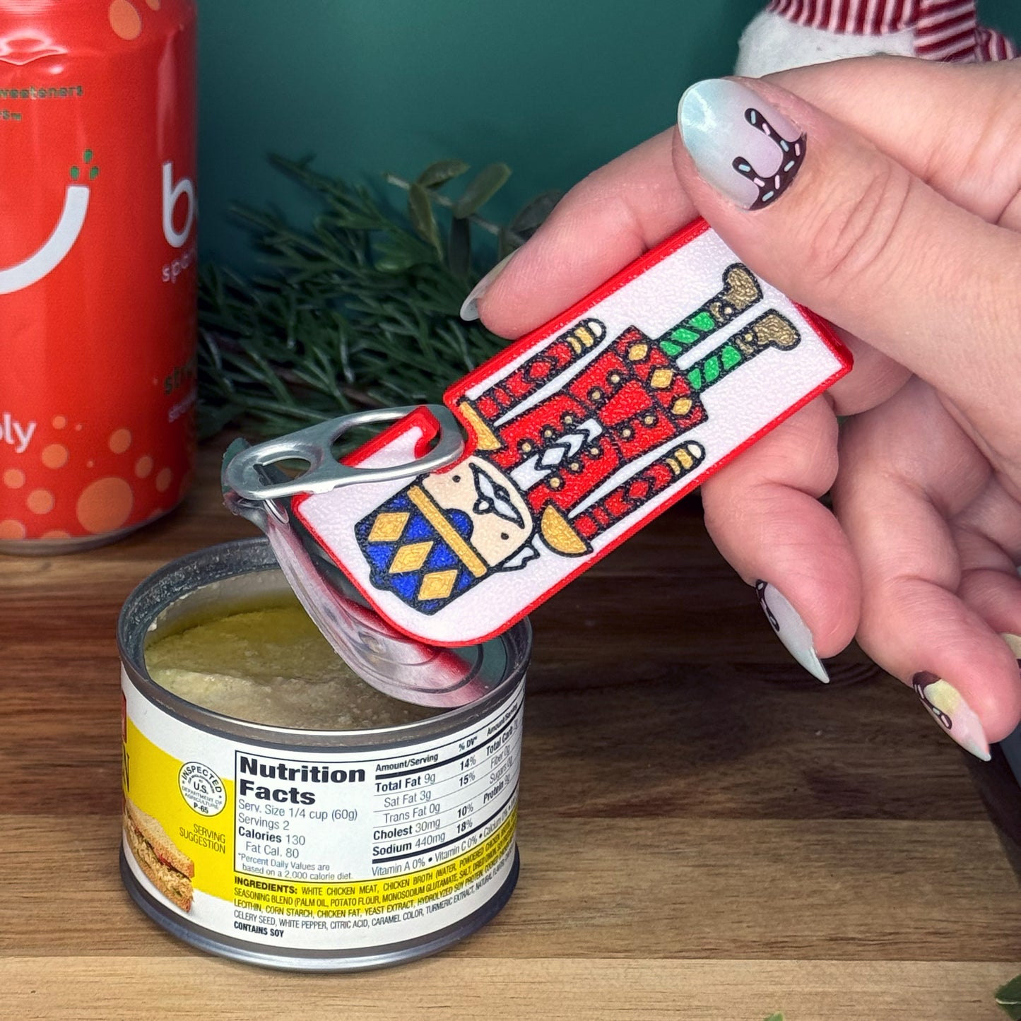 Hand using a Tab Buddy XL with a colorful nutcracker design on a can of food.