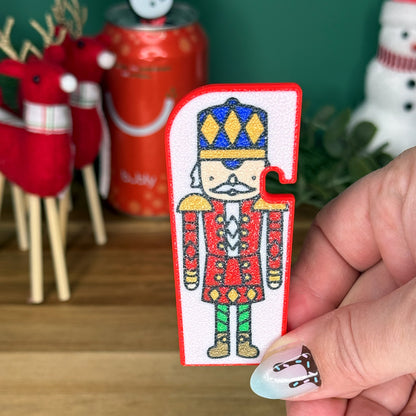 Hand holding a Nutcracker Tab Buddy XL with Christmas decorations in the background
