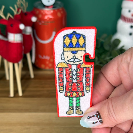 Hand holding a Nutcracker Tab Buddy XL with Christmas decorations in the background