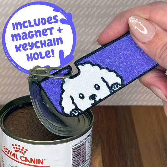 A White Poodle-inspired Tab Buddy XL is used to peel back the lid of a can of dog food. Descriptive text reads "Includes Magnet + Keychain Hole!"