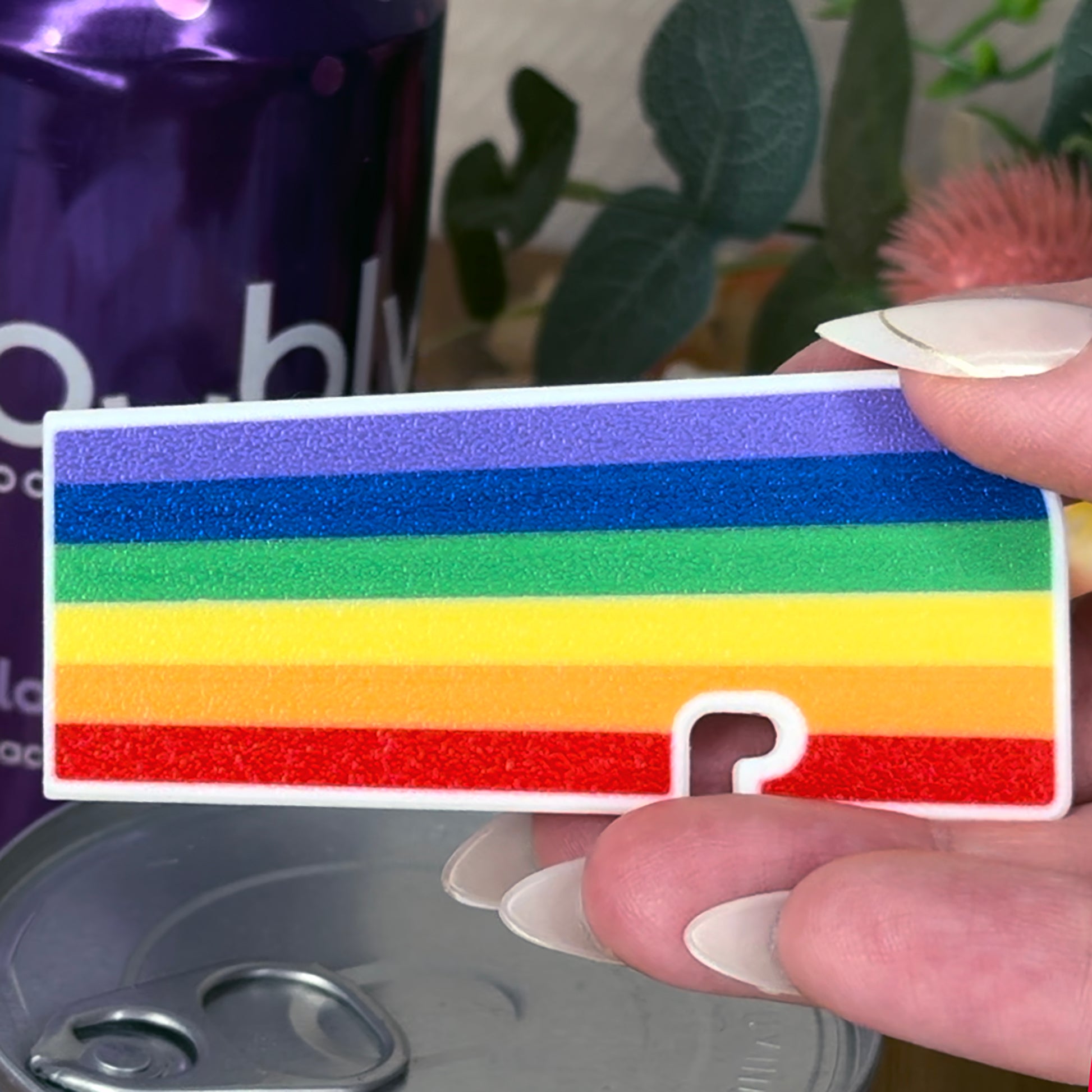 Rainbow striped Tab Buddy XL with a held by a hand, blurred background