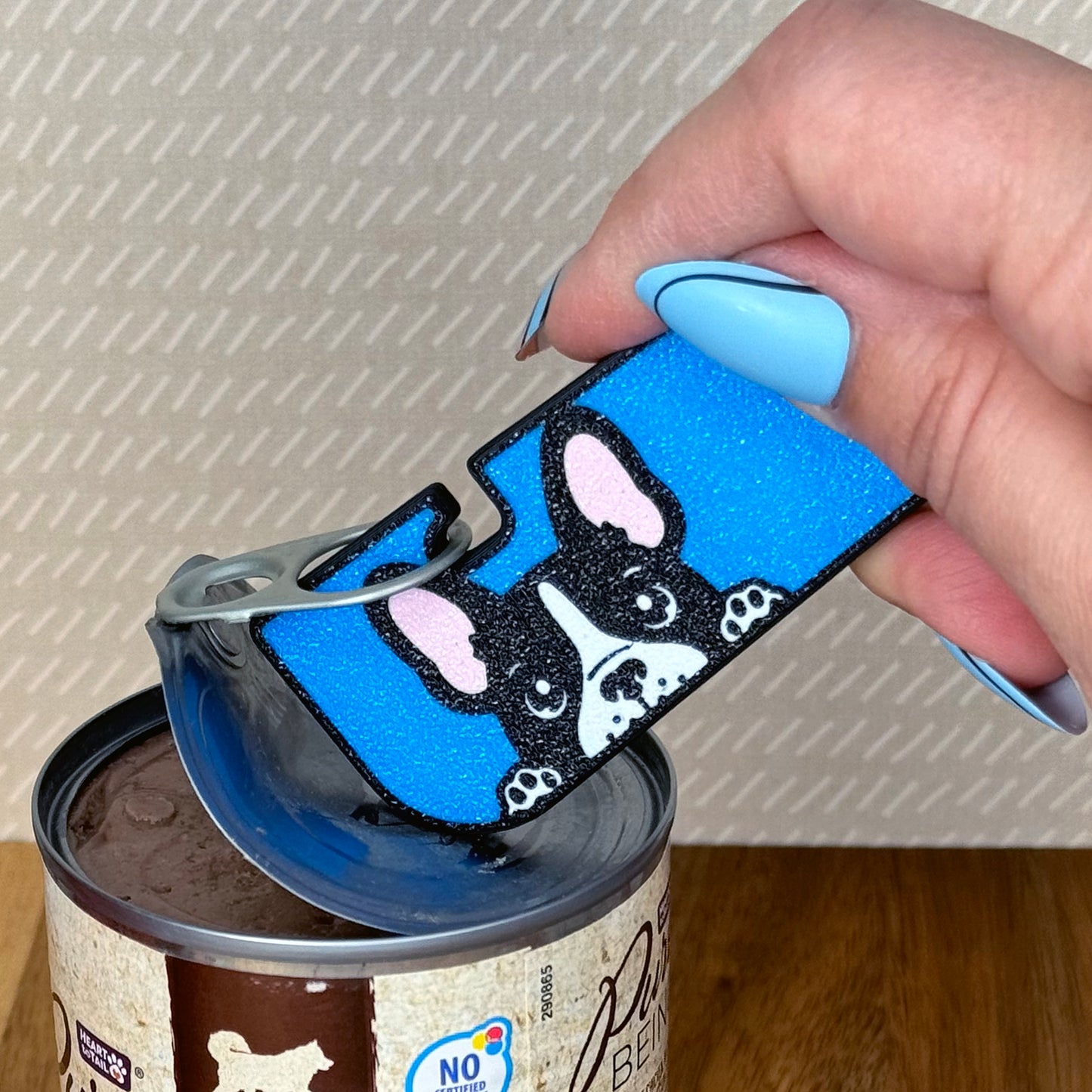 Hand using a blue dog-themed Tab Buddy XL on a can.