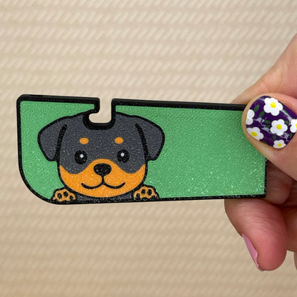 Hand holding a Tab Buddy XL with a cute Rottweiler dog design and green background on its surface. A tan surface is in the background of the photo.