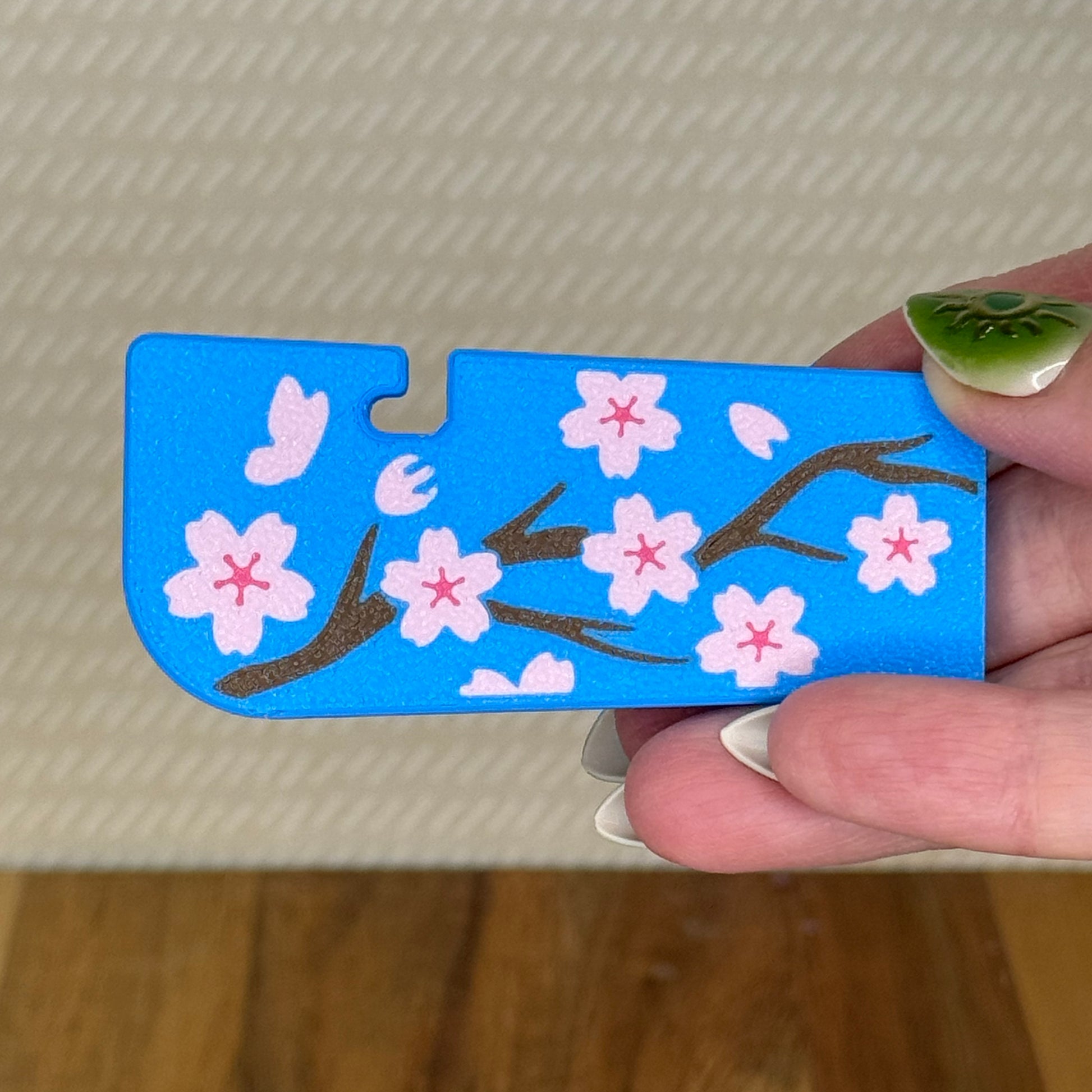 A Tab Buddy XL with a pink cherry blossom design against a blue background is held in a hand.