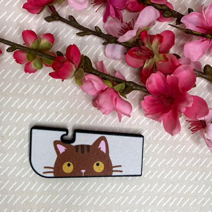 A Tab Buddy XL in Sneaky Brown Tabby Cat color variation rests atop a beige surface with cherry blossom flowers in background.