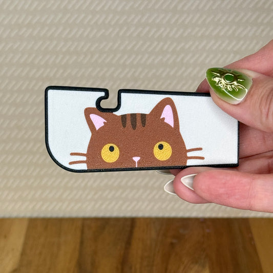 A sneaky cat Tab Buddy XL is held in a hand against a beige background. The cat is a golden-eyed brown tabby peeking up along the edge of the XL with a cream background. 