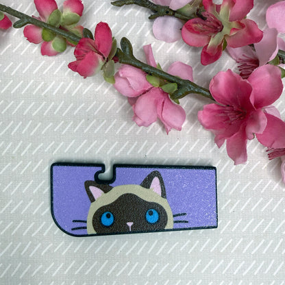 A Tab Buddy XL in Sneaky Siamese Cat color variation rests atop a beige surface with cherry blossom flowers in background.