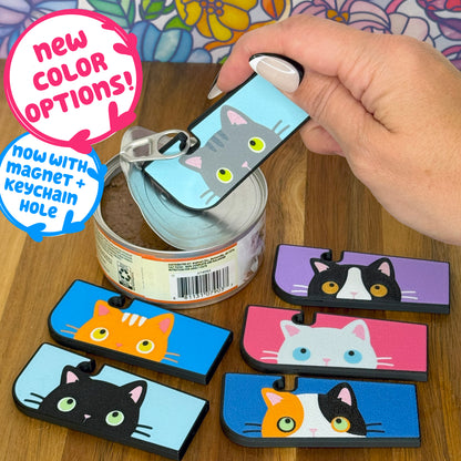 Cat-themed Tab Buddies can openers with colorful designs on a wooden surface